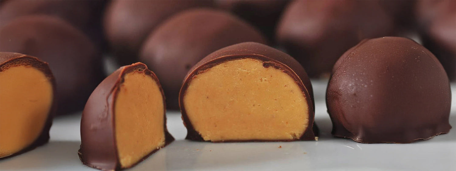 Close-up of no-bake chocolate peanut butter protein balls, with one cut in half showing the creamy peanut filling coated in a smooth dark chocolate shell.