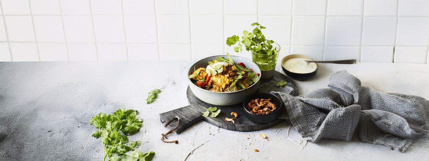 Bowl of chicken korma garnished with fresh coriander, served with cashews and sauce on a rustic table setting.