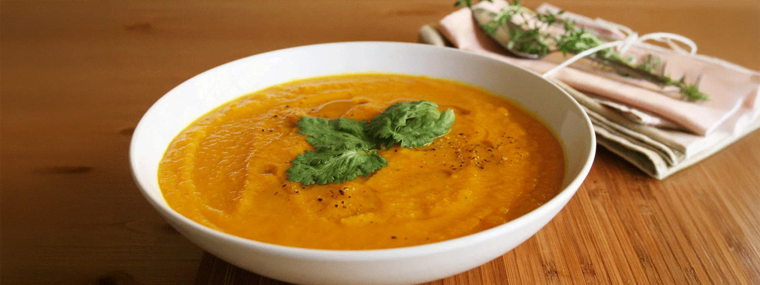 Bowl of cleansing ginger, carrot, and sweet potato soup garnished with fresh coriander on a wooden table