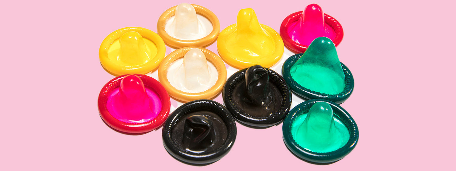 Flat lay of colourful condoms arranged on a pink background with bold text overlay reading ‘Safe Sex Just Got Smarter – Condoms that change colour the second they hit an STI, plus anti-aging lube and digital firewalls.