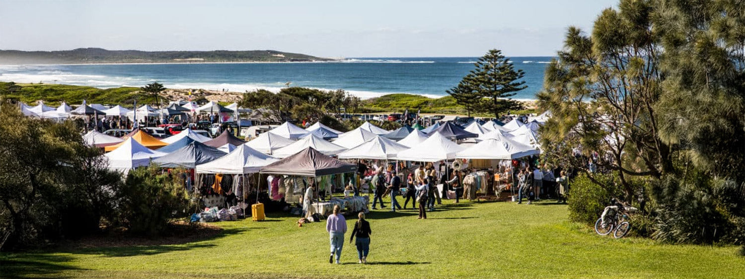 Outdoor stalls at Cronulla Winter Markets 2025 at Don Lucas Reserve, with crowds browsing under white tents near the beach.
