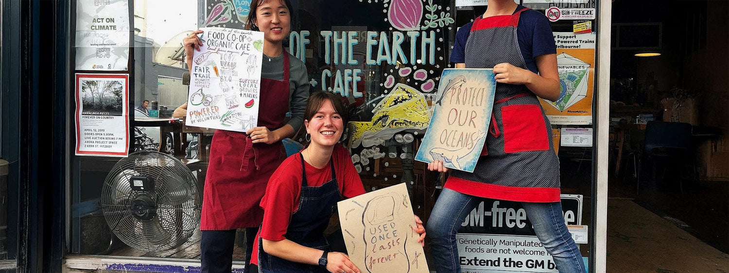 Friends of the Earth Melbourne volunteers outside the Collingwood Food Co-op & Café holding eco-activism signs promoting organic, vegan, waste-free living.