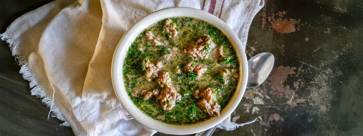 Organic beef and kale instant pot soup served in a rustic white bowl, topped with tender ground beef and fresh kale in a rich broth.