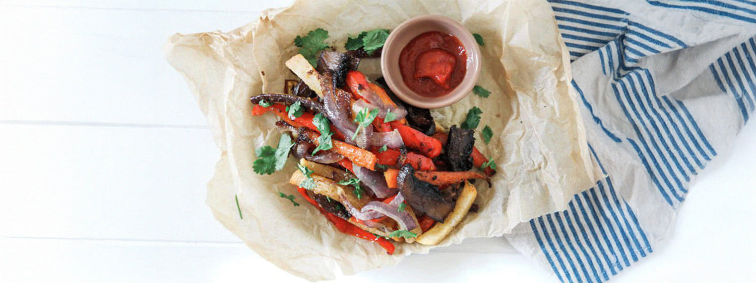 Baked root vegetable chips with carrots, beetroot, onions, and capsicum, served on parchment paper with fresh herbs and dipping sauce.