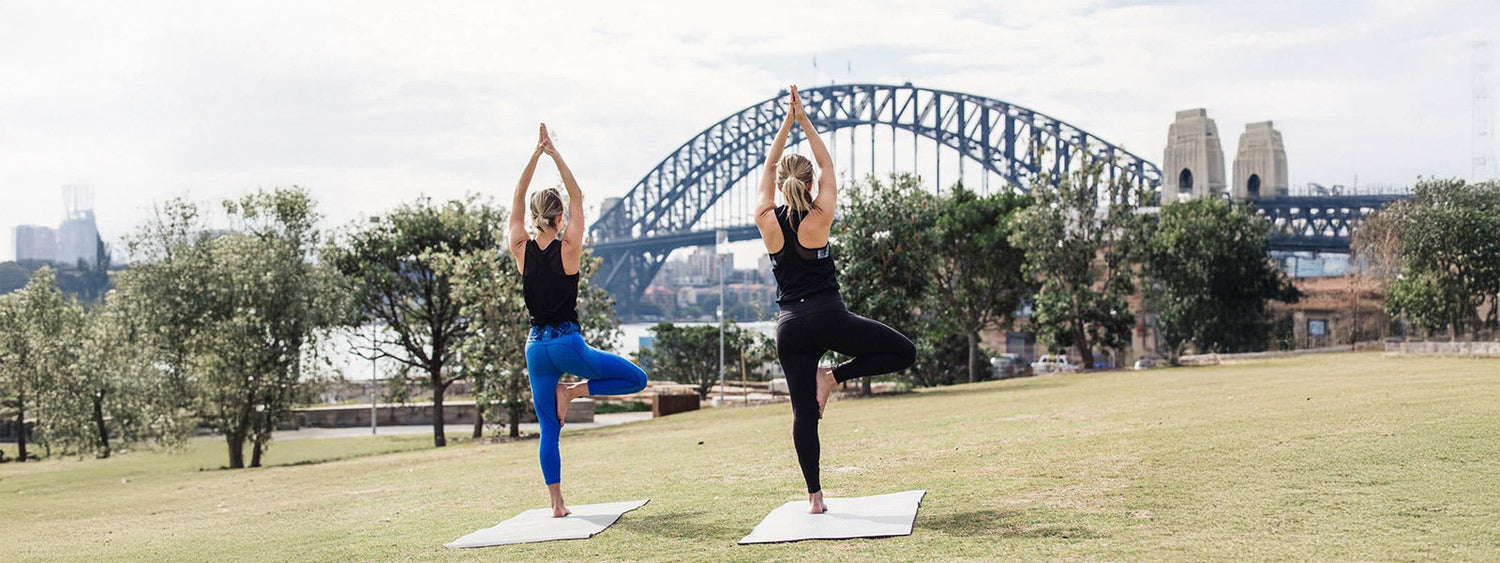Two women doing sunrise yoga on grass with Sydney Harbour Bridge in the background during Barangaroo You Wellness Month