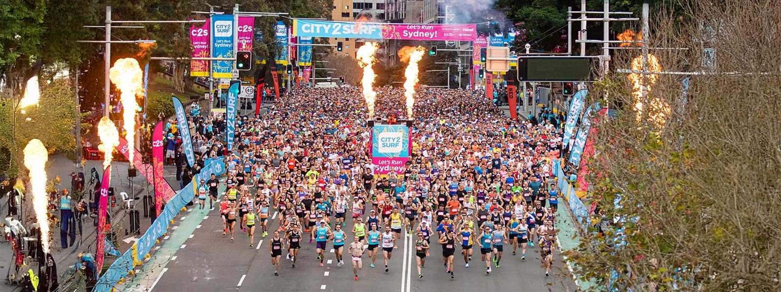 Thousands of runners at the City2Surf 2025 start line in Sydney, with fireworks and banners at Hyde Park
