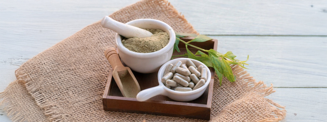Herbal supplement capsules in a ceramic bowl with powdered supplement in a mortar and pestle on a wooden tray, natural wellness flat lay.