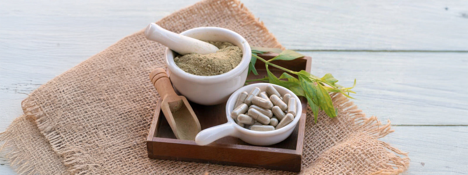 Herbal supplement capsules in a ceramic bowl with powdered supplement in a mortar and pestle on a wooden tray, natural wellness flat lay.
